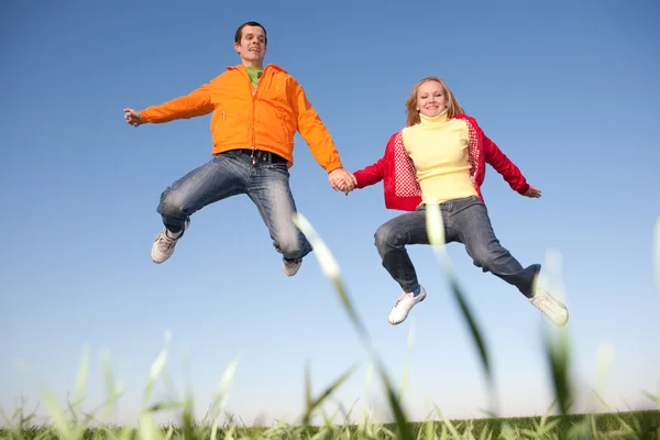 緑の牧草地の上空で跳んで幸せな笑みを浮かべてカップル — ストック写真