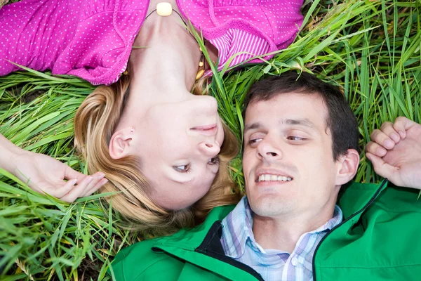 Young love couple lay on the green grass outdoors. — Stock Photo, Image