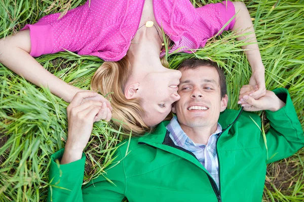 Young love couple lay on the green grass outdoors. — Stock Photo, Image