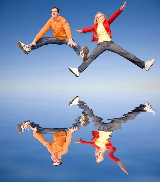 Feliz casal sorrindo pulando no céu. Reflexo na água — Fotografia de Stock