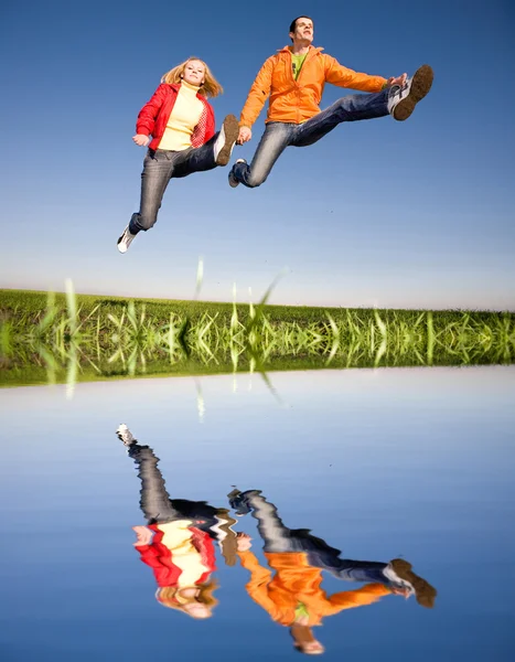 Felice coppia sorridente saltando nel cielo blu — Foto Stock