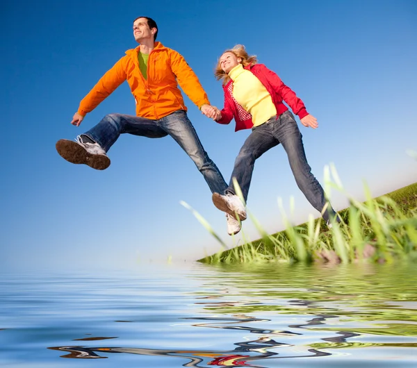 Счастливая улыбающаяся пара, прыгающая в небо над зеленым лугом. Восстановление — стоковое фото