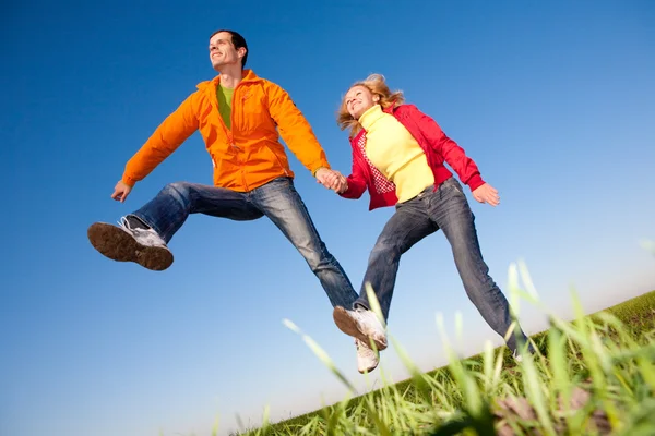 Joyeux couple souriant sautant dans le ciel au-dessus d'une prairie verte — Photo