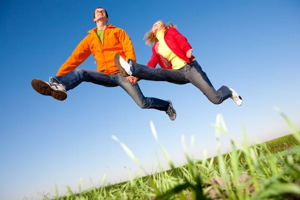 Šťastný usmívající se pár skákání na obloze nad zelenou louku — Stock fotografie