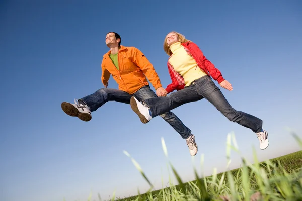 Gelukkige lachende paar springen in de hemel boven een groene weide — Stockfoto