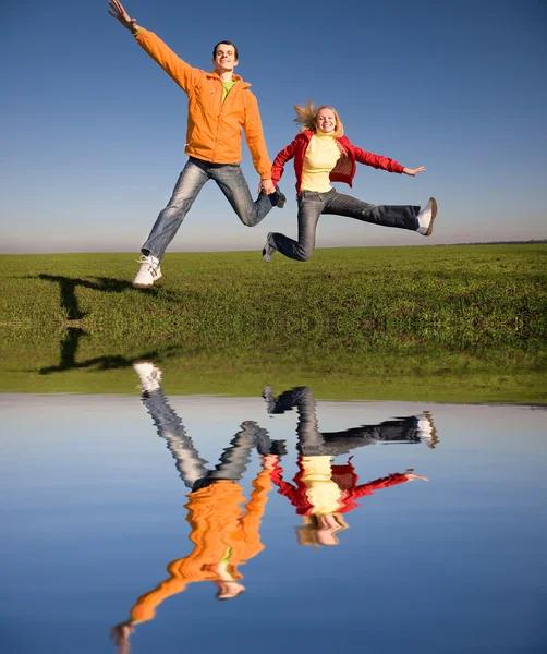 Šťastný mladý pár skákání na obloze nad zelenou louku — Stock fotografie