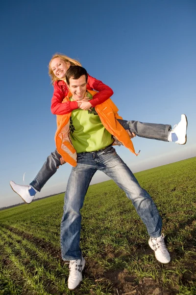 緑の牧草地の上空で跳んで幸せな笑みを浮かべてカップル — ストック写真