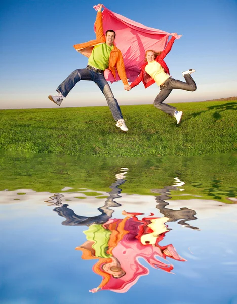 在绿色 meadow.reflecte 头顶上的天空中跳跃的快乐年轻夫妇 — 图库照片