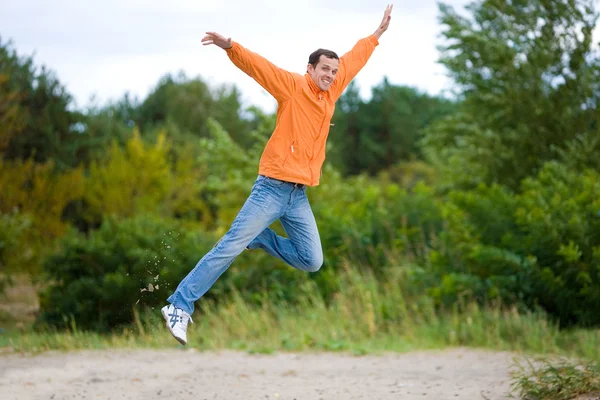 Szczęśliwy młody człowiek - skoki na niebie przed zielonym drzewem — Zdjęcie stockowe