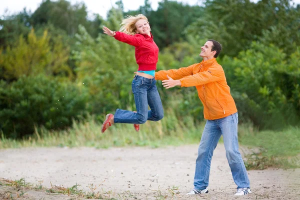 Boldog, fiatal pár - szemben a zöld fa ugrás — Stock Fotó