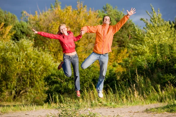 Feliz joven pareja - saltando en el cielo por encima de un trío naranja-verde — Foto de Stock