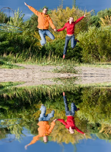 Happy Young Couple - saltare nel cielo contro una t verde arancio — Foto Stock
