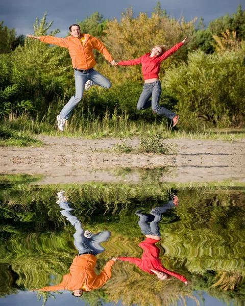 Casal Jovem Feliz - pulando no céu contra uma árvore verde — Fotografia de Stock