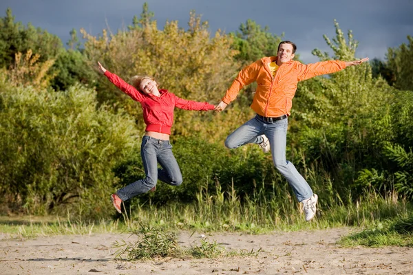 Casal Jovem Feliz - pulando no céu contra uma árvore verde — Fotografia de Stock