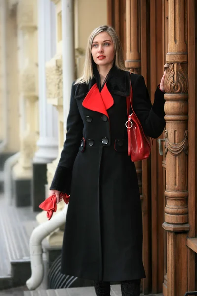 Mooie jonge vrouw in een zwarte jas staat op een stap Stockfoto