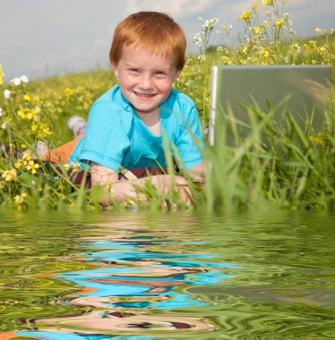 Smiling child with laptop computer on meadow. Reflected in Water. clipart