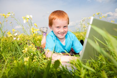 Smiling child with laptop computer on meadow clipart