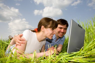 bir dizüstü bilgisayarda açık havada rahat mutlu çift. Yeşil çimenlerin üzerinde yatıyordu.
