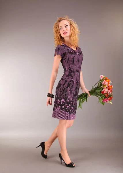 Piękna młoda kobieta w świetle sukni z kwiatami na szarym tle — Zdjęcie stockowe