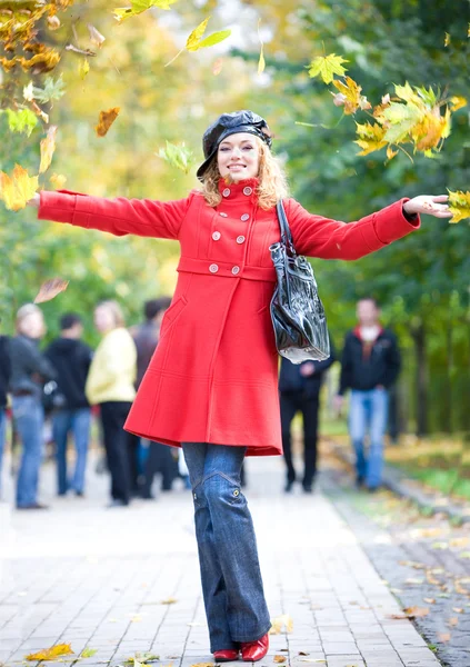 Femme heureuse en rouge jetant des feuilles dans l'air — Photo