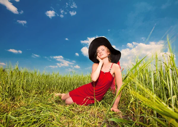 Szczęśliwa młoda kobieta siedzi na trawie w kapeluszu — Zdjęcie stockowe