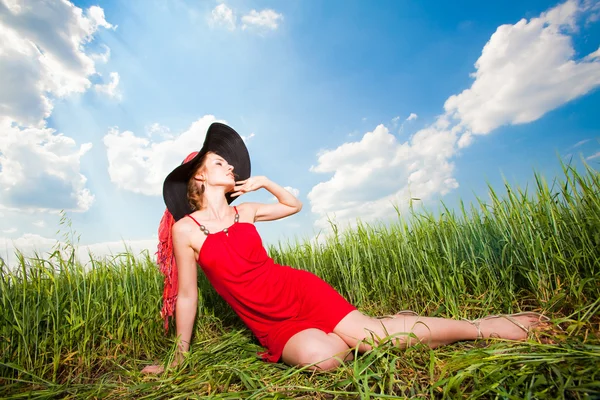 Szczęśliwa młoda kobieta siedzi na trawie w kapeluszu — Zdjęcie stockowe