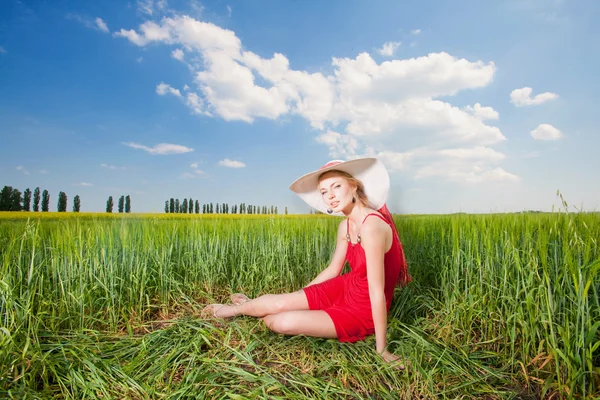 Dívka v klobouku sedí na trávě — Stock fotografie