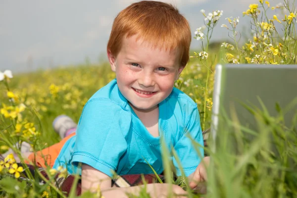 Niño sonriente con computadora portátil en el prado —  Fotos de Stock
