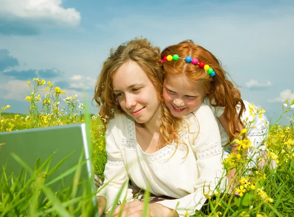 Mother and daughter lay on a grass with a notebook — Stock Photo, Image
