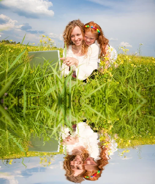 Mor och dotter låg på ett gräs med en bärbar dator — Stockfoto