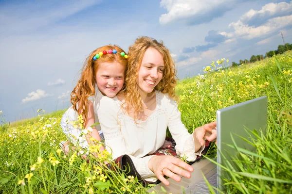 妈妈和女儿带着笔记本电脑躺在草地上 — 图库照片