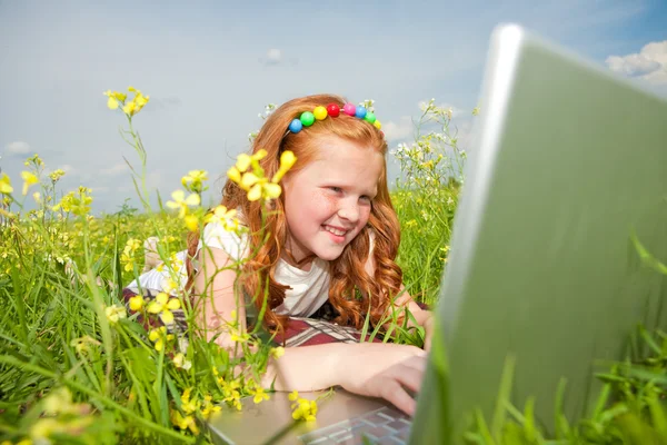 Meisje met laptop rusten op weide. — Stockfoto