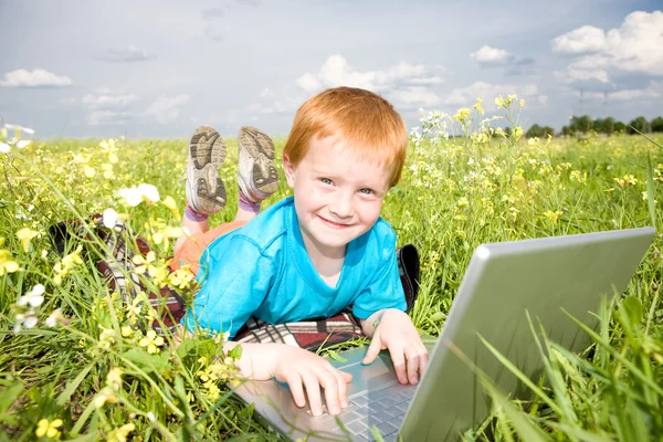 Niño sonriente con computadora portátil en el prado — Foto de Stock