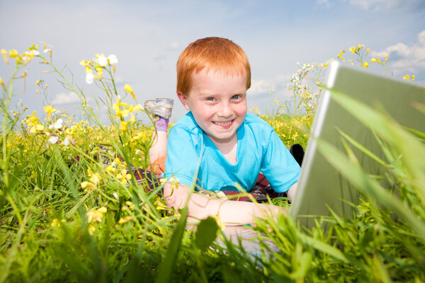 Smiling child with laptop computer on meadow