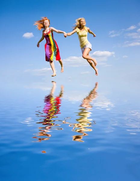 Két vidám fiatal lányok menekülnek a víz, a kék ég alatt. — Stock Fotó