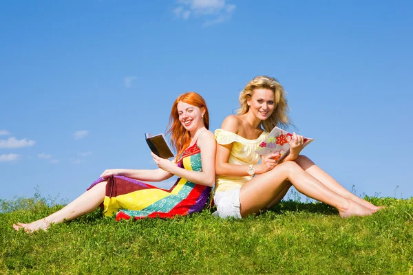 Twee mooie meisjes met notitieboekje buitenshuis. zittend op de groene — Stockfoto