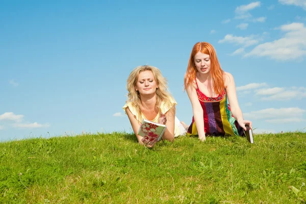 Two beautiful girls with notebooks outdoors. Lay on the green gr — Stock Photo, Image