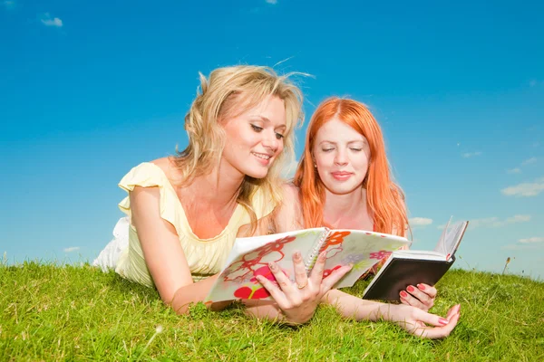 Two beautiful girls with notebooks outdoors. Lay on the green gr — Stock Photo, Image