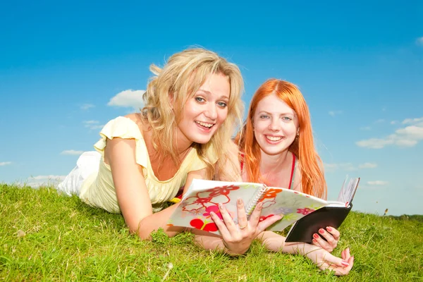 两个漂亮的女孩与户外的笔记本 躺在绿草地上 — 图库照片
