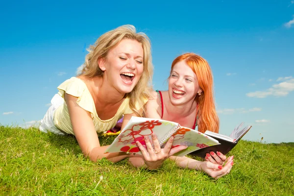 两个漂亮的女孩与户外的笔记本 躺在绿草地上 — 图库照片