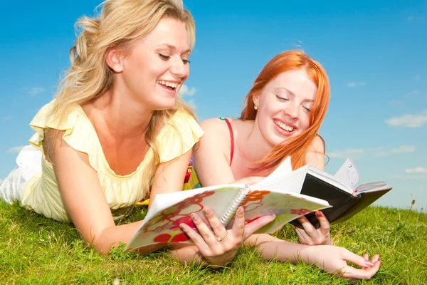 Dos hermosas chicas con cuadernos al aire libre. Acuéstese en el gr verde —  Fotos de Stock