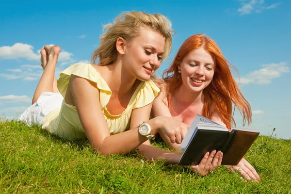 屋外のノートブックを 2 つの美しい女の子。グリーン gr に横たわっていた — ストック写真