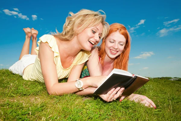 Dwie piękne dziewczyny z notebooków na zewnątrz. leżał na gr zielony — Zdjęcie stockowe