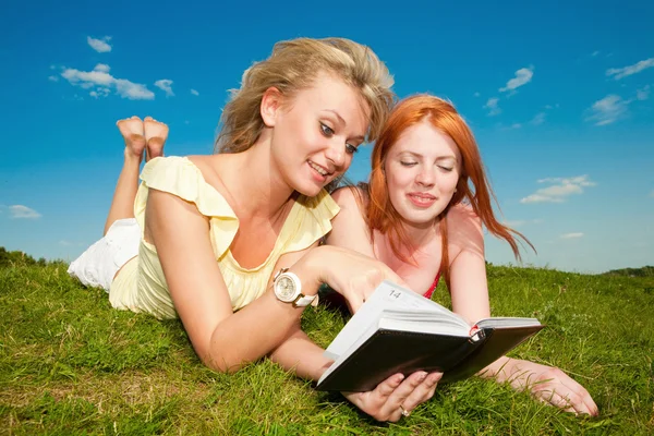 Twee mooie meisjes met laptops buitenshuis. Leg op de groene gr — Stockfoto