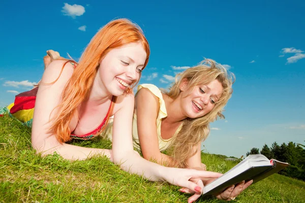 Zwei schöne Mädchen mit Notizbüchern im Freien. lag auf dem grünen Gras — Stockfoto
