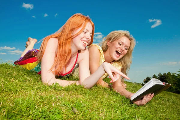 Två vackra flickor med bärbara datorer utomhus. låg på den gröna gr — Stockfoto