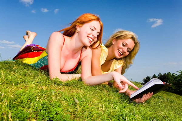 Δύο όμορφα κορίτσια με το σημειωματάριο σε εξωτερικούς χώρους. Lay για το πράσινο παιχνίδι — Φωτογραφία Αρχείου