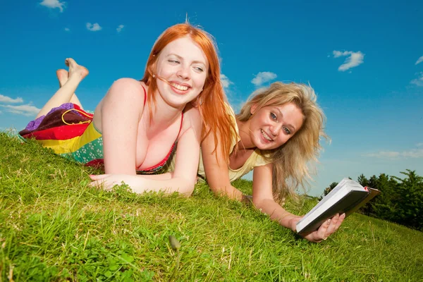 Dos hermosas chicas con cuadernos al aire libre. Acuéstese en el gr verde —  Fotos de Stock