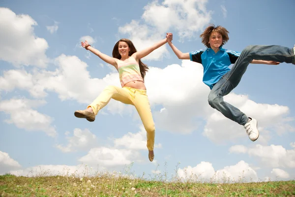 Chica y niño saltando en el prado sonriendo bajo el cielo azul —  Fotos de Stock