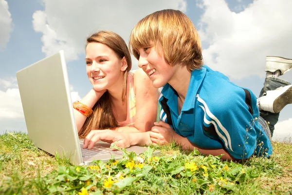 Dva usmívající se teenageři s notebookem na louce. — Stock fotografie